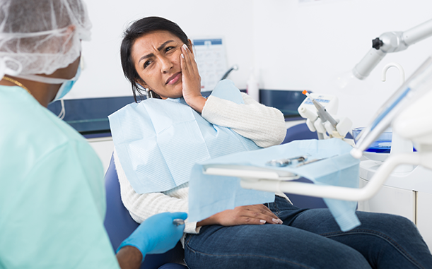 An adult, representing a Hispanic ALICE patient, sits in a dentist’s chair holding their cheek in pain.