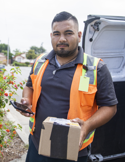 A delivery driver in an orange vest delivers a package to a residential address. 